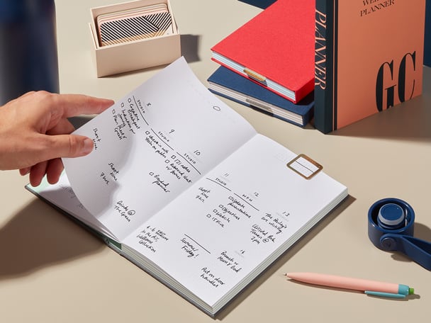 Open Planner featuring a Brass Clip on a desk with a hand turning the page